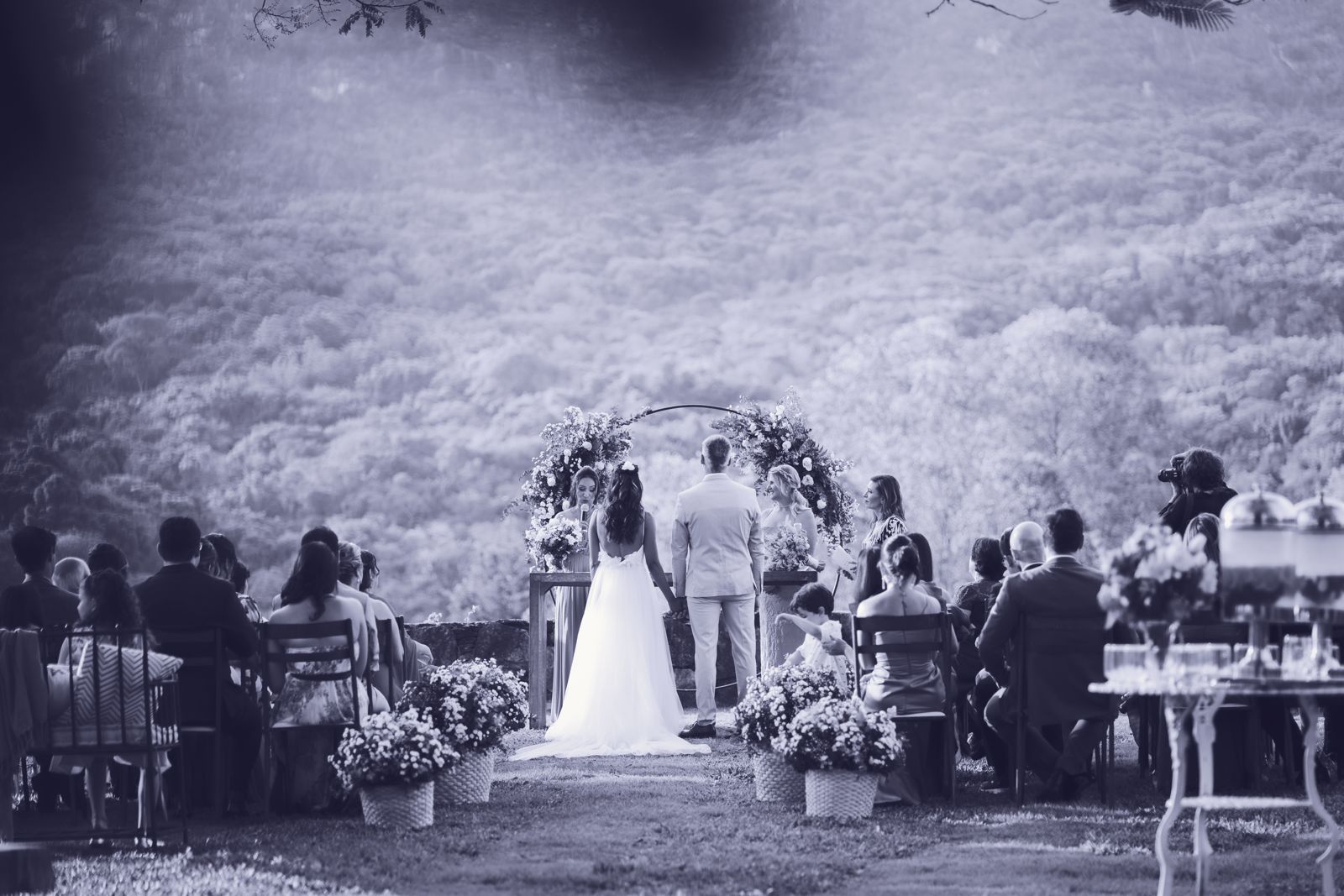 Cérémonie de mariage en plein air, les mariés de dos devant l'arche fleurie, entourés de leurs invités